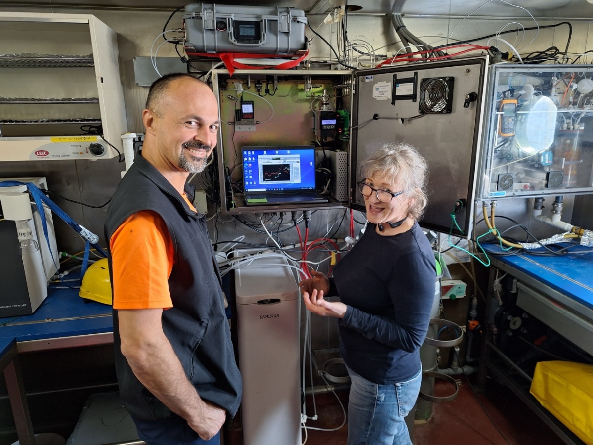 two scientists in front of computer looking at the camera smiling