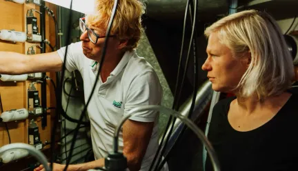 Two people standing next to each other are looking to the left at measuring instruments.